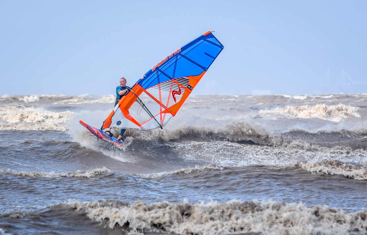 Windsurfer riding the waves holding onto a red, white and blue sail